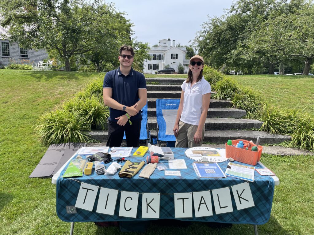 Kyle and Lea stand smiling behind a table of tick information.